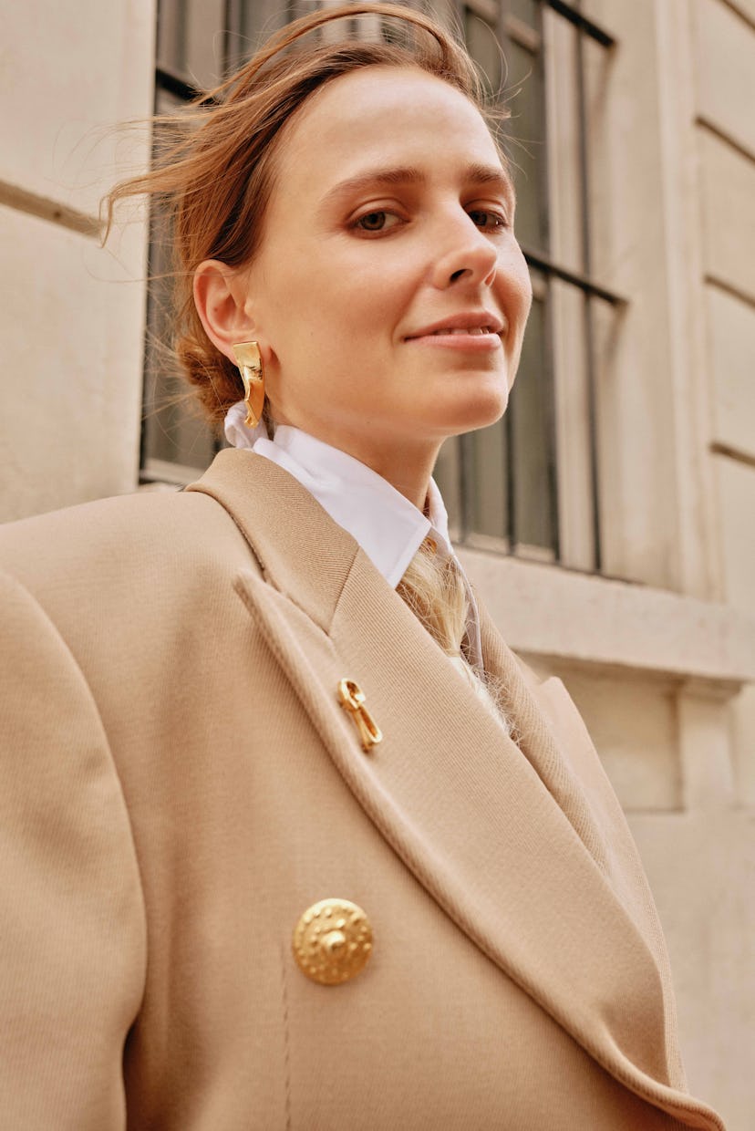 A woman in a stylish beige oversized blazer and white shirt poses confidently outdoors, adorned with...