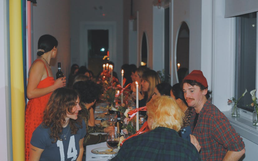People socializing at a dinner party decorated with a long table covered in candles, enjoying conver...