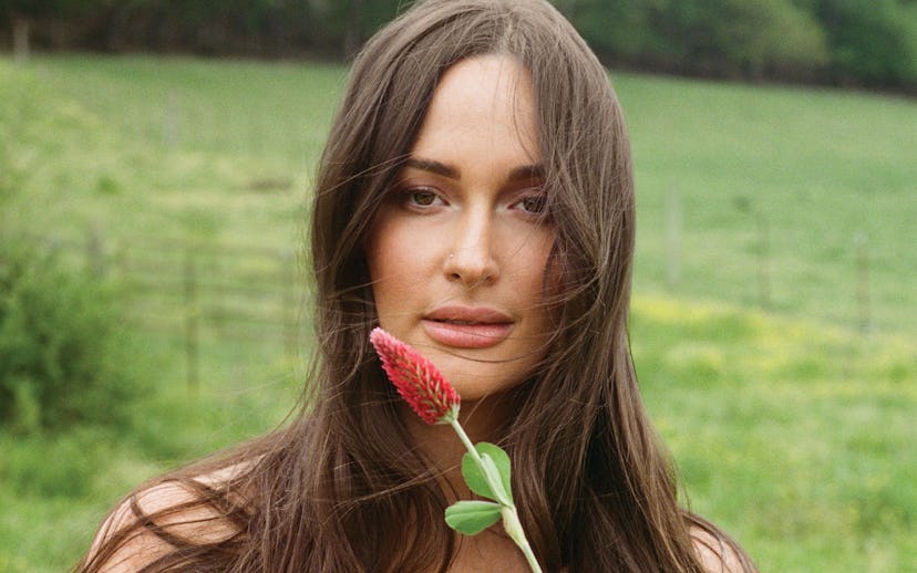 A woman holds a red flower to her face in a field, with text "DEEPER WELL" in the upper right.