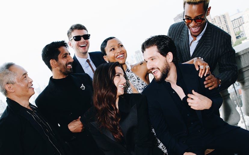 A lively group photo of seven people, dressed stylishly, laughing and interacting in a bright outdoo...